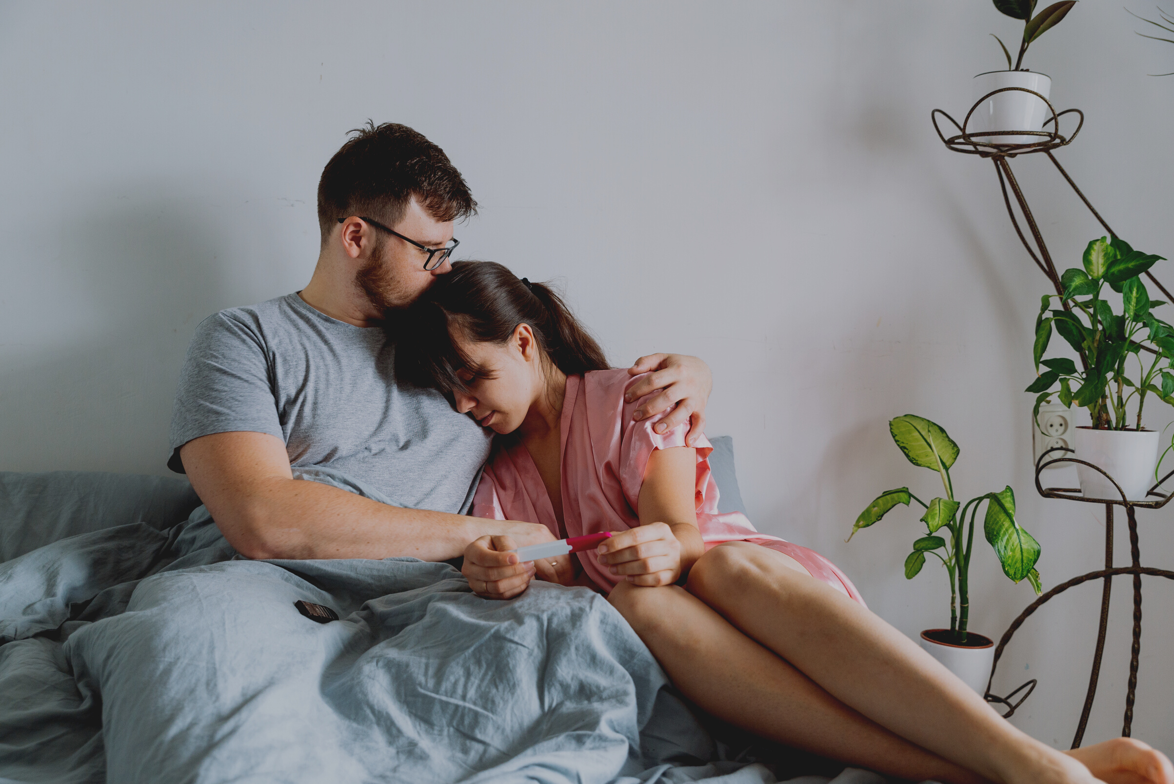 sad couple in bed looking at negative pregnancy test